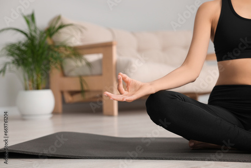 Woman practicing Padmasana on yoga mat at home, closeup and space for text. Lotus pose