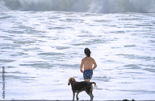 Young man and beagle dog having bath in waves on sand beach photo