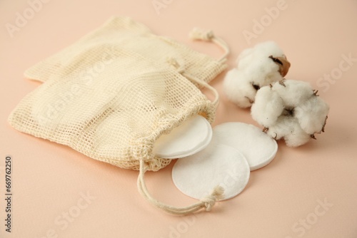 Bags with cotton pads and flowers on beige background, closeup