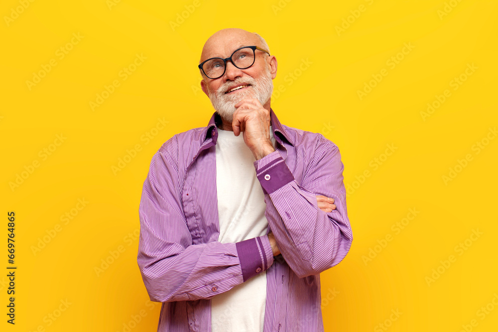 pensive old bald grandfather with gray beard in eyeglasses stands with his arms crossed on yellow isolated background pensive old bald grandfather with gray beard in eyeglasses stands with his arms crossed on yellow isolated background