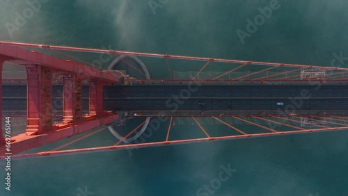 Cinematic top view of San Francisco in misty golden sunset light. View from top to bottom cars driving by road on tall red construction bridge of California landmark USA. Golden Gate Bridge overhead