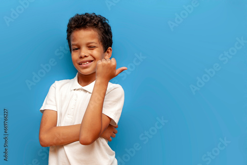 african american teenage boy pointing with hand back on blue isolated background, curly schoolboy advertising © Богдан Маліцький