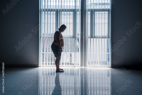 Asian 30s overweight man weighing himself with a scale