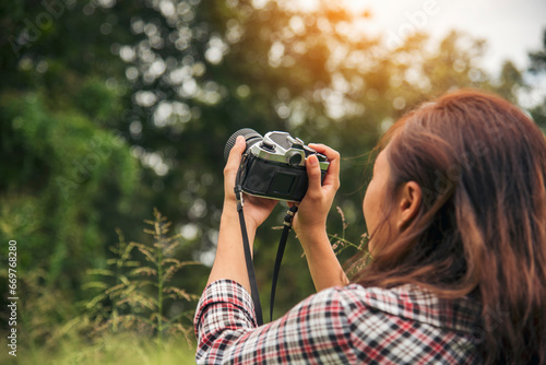 Asian Women with vintage film camera take a photo. Smiling female photographer look at photo from professional camera outdoor. Young woman shooting photo in green nature park. Beautiful woman hobby