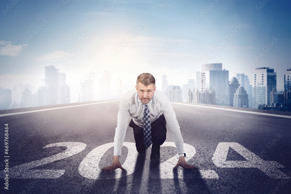 Caucasian businessman ready to chase his dream while kneeling on the start line with numbers 2024 Caucasian businessman ready to chase his dream while kneeling on the start line with numbers 2024