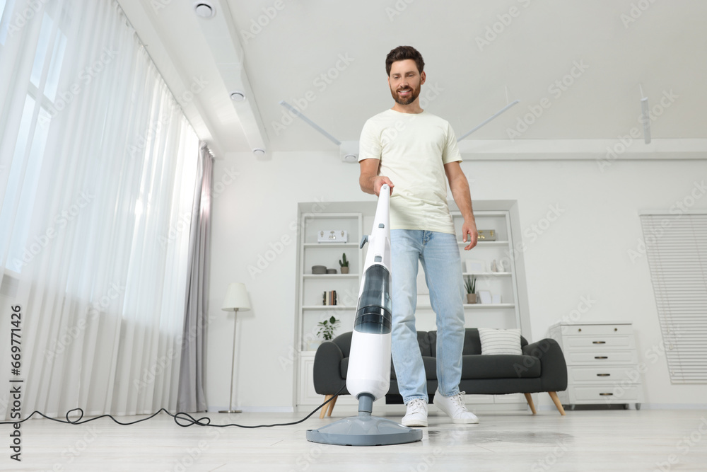 Fototapeta premium Happy man cleaning floor with steam mop at home, low angle view