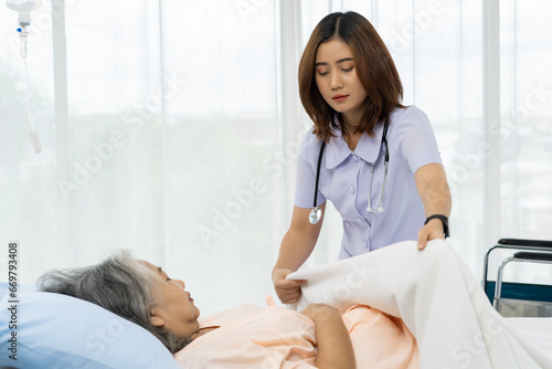 A nurse or caregiver of an elderly patient is helping to cover blanket a patient lying in bed.