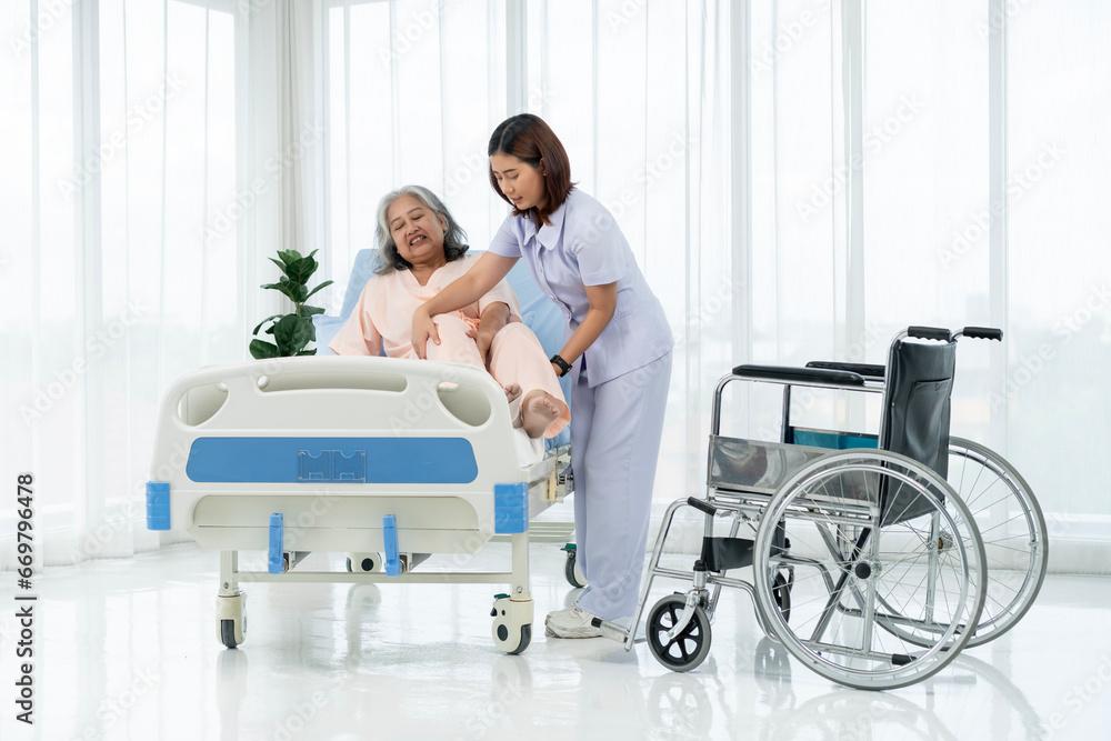 A nurse carries an elderly Asian patient from a wheelchair onto a bed after taking him for an x-ray of his leg injured in an accident. A nurse carries an elderly Asian patient from a wheelchair onto a bed after taking him for an x-ray of his leg injured in an accident.