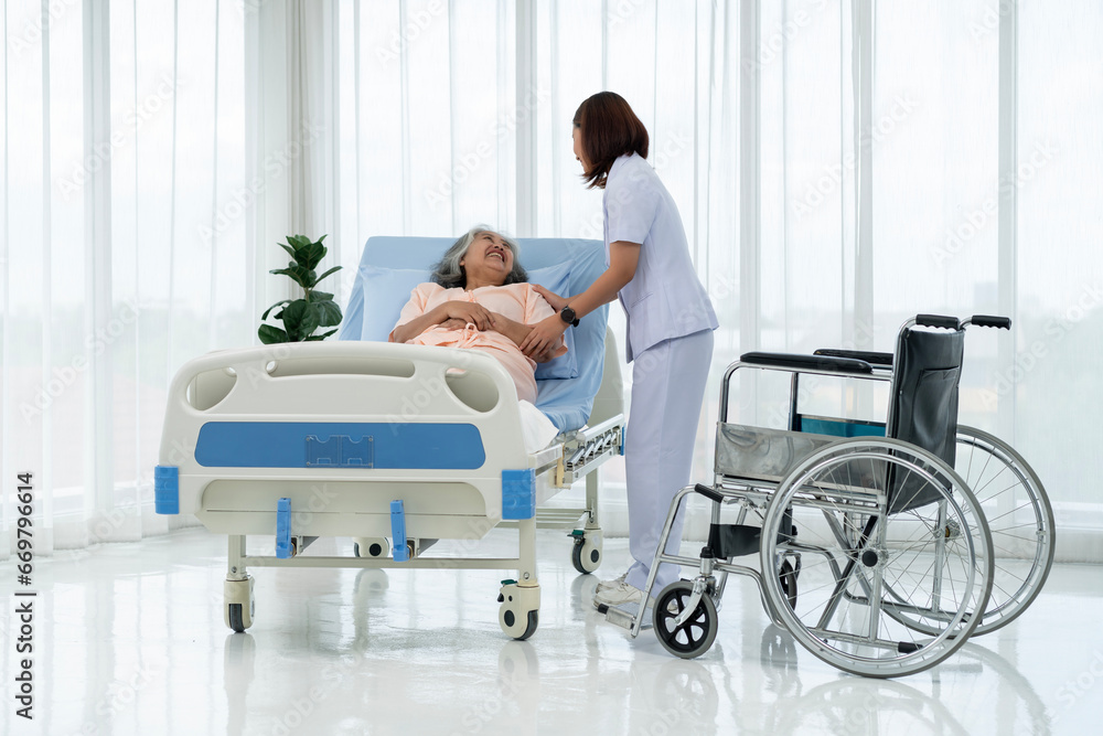 A nurse carries an elderly Asian patient from a wheelchair onto a bed after taking him for an x-ray of his leg injured in an accident. A nurse carries an elderly Asian patient from a wheelchair onto a bed after taking him for an x-ray of his leg injured in an accident.
