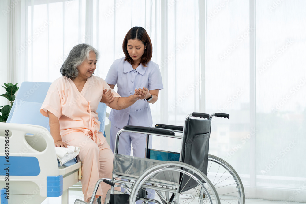 A nurse carries an elderly Asian patient into a wheelchair to take him to get an x-ray of his leg injured in an accident. A nurse carries an elderly Asian patient into a wheelchair to take him to get an x-ray of his leg injured in an accident.