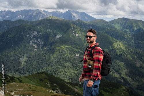 A male traveler in sunglasses with a briefcase behind his back high in the Polish Tatra Mountains in summer.