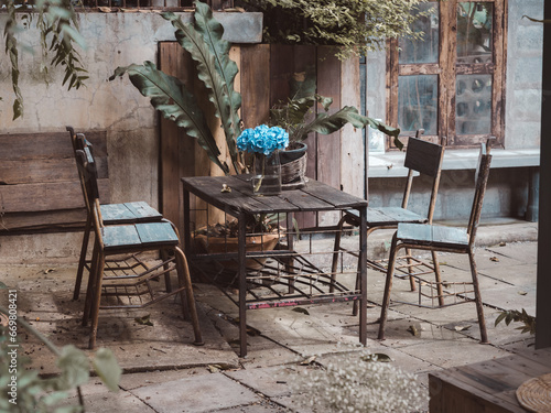 Lively fresh blue flowers in vintage glass bottle standing alone on wooden dining table with empty chairs decoration in abandoned old house. Hope, life survival and beauty of nature concepts.