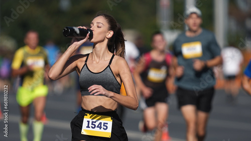 Woman athlete drinking water bottle. Thirsty people run long distance. Girl sport runner work out. Adult person train public park. Thirst jogger take break. Jog city arena. Sprinter sip fresh shake. photo