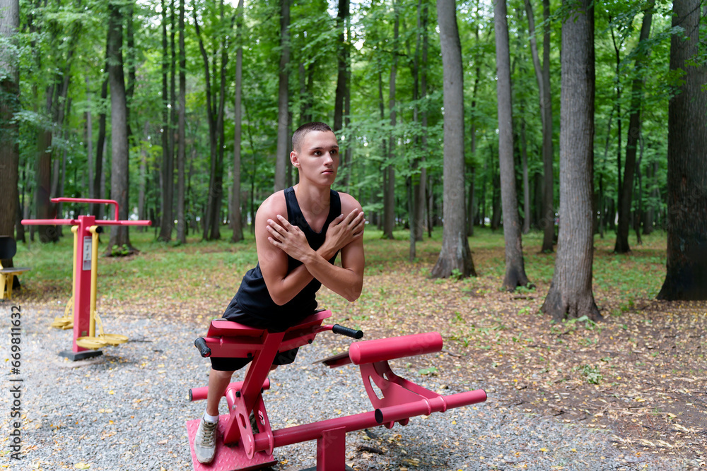 A young man leads a healthy lifestyle and does physical activity on outdoor exercise equipment in a city forest park.