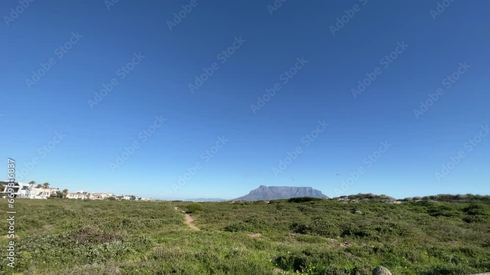 Beach footpaths on a grassy sandy shoreline with houses and apartments on the beach with views of Table Mountain Beach footpaths on a grassy sandy shoreline with houses and apartments on the beach with views of Table Mountain