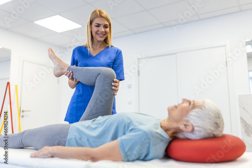 close up of female physiotherapist is helping senior elder woman stretching her hamstring and doing thigh or leg rehabilitation in exercise room - she is lying on massage bed