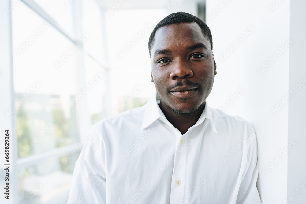 Young african man in white shirt and glasses posing near large window Young african man in white shirt and glasses posing near large window