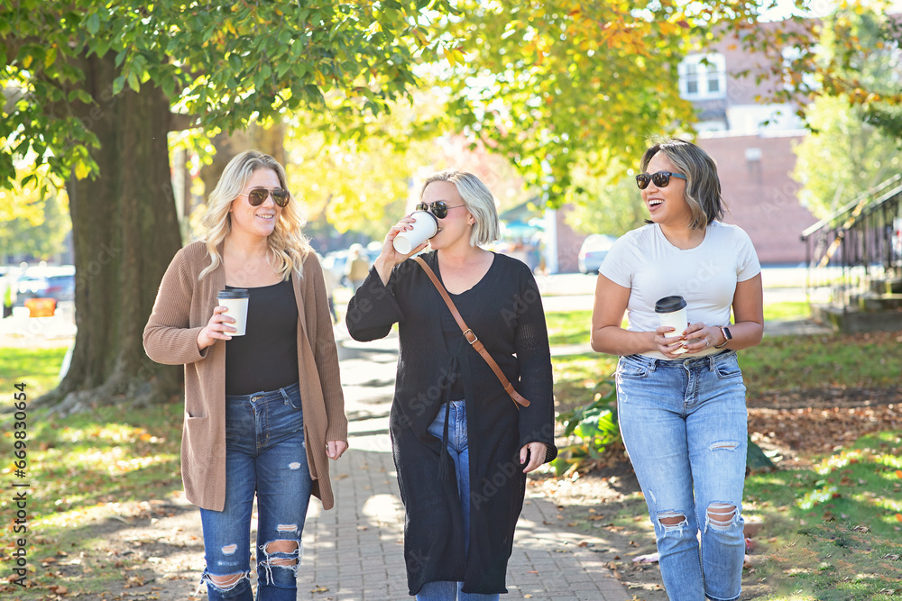Three women walking down Main Street drinking coffee; friendship
