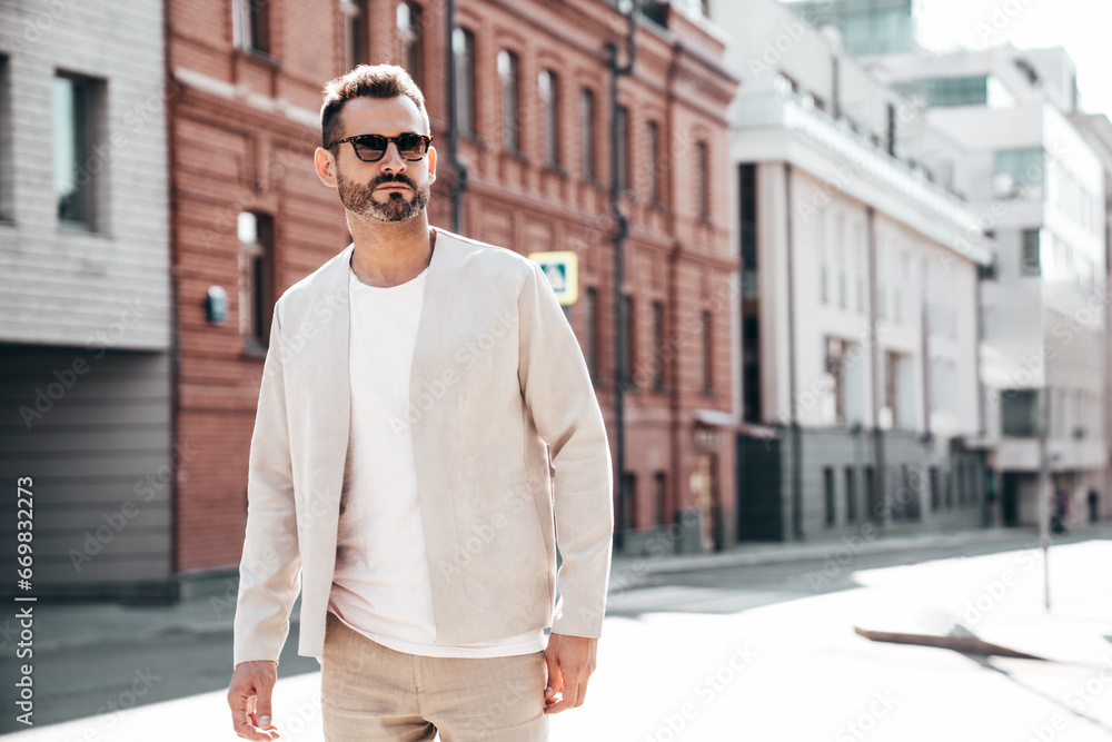 Fototapeta premium Portrait of handsome confident stylish hipster lambersexual model. Sexy modern man dressed in elegant suit. Fashion male posing in the street background in Europe city at sunset. In sunglasses