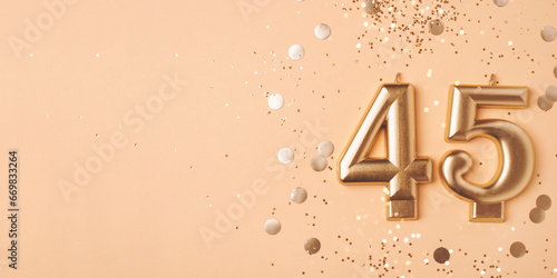 45 years celebration. Greeting banner. Gold candles in the form of number forty five on peach background with confetti. photo