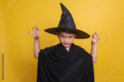 Portrait of Asian little boy wearing witch costume gesturing scary faces in Halloween celebration.