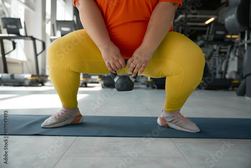 Crop of overweight obese woman squatting with kettlebell while training at gym