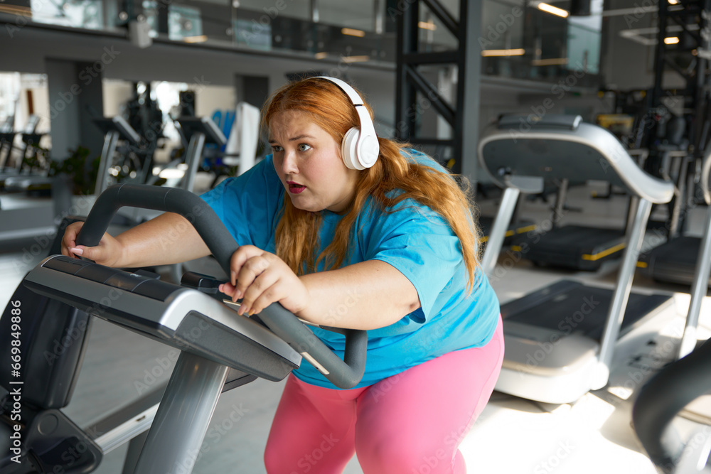 Fototapeta premium Crazy motivated overweight woman riding fast on stationary bike