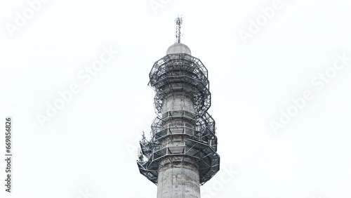 Aerial low angle ascending shot of a bleak industrial concrete television and radio link tower in Pasila, Helsinki, Finland on a bright and foggy day. Sky and apartment buildings in background. photo