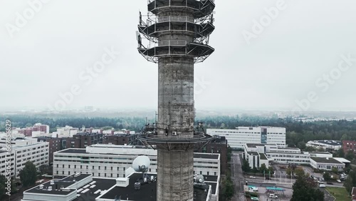 Aerial medium shot of a bleak industrial concrete television and radio link tower in Pasila, Helsinki, Finland on a bright and foggy day. Camera ascending, apartment buildings in background. photo