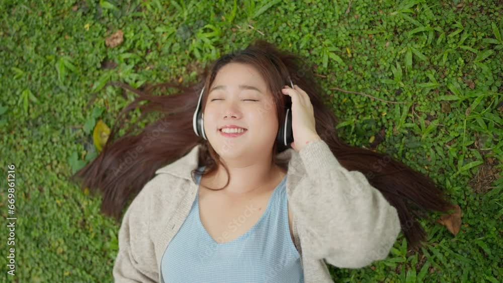 Close up face of beautiful young Asian woman wearing headphones enjoy listening to music while laying on grass at the park. Lovely girl enjoying music while laying on the grass. Lifestyle concept Close up face of beautiful young Asian woman wearing headphones enjoy listening to music while laying on grass at the park. Lovely girl enjoying music while laying on the grass. Lifestyle concept
