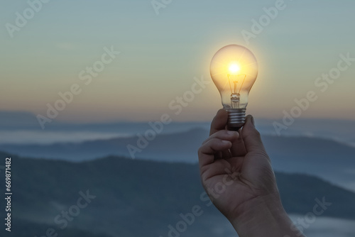 Close up electric light bulbs and switch on to yellow lights glowing on blurred and bokeh reflection lighting background. Hand holding light bulb. Lamp idea concept with innovation and inspiration.