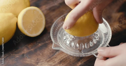 Female hand squeezes fresh lemon juice on glass squeezer in close up photo
