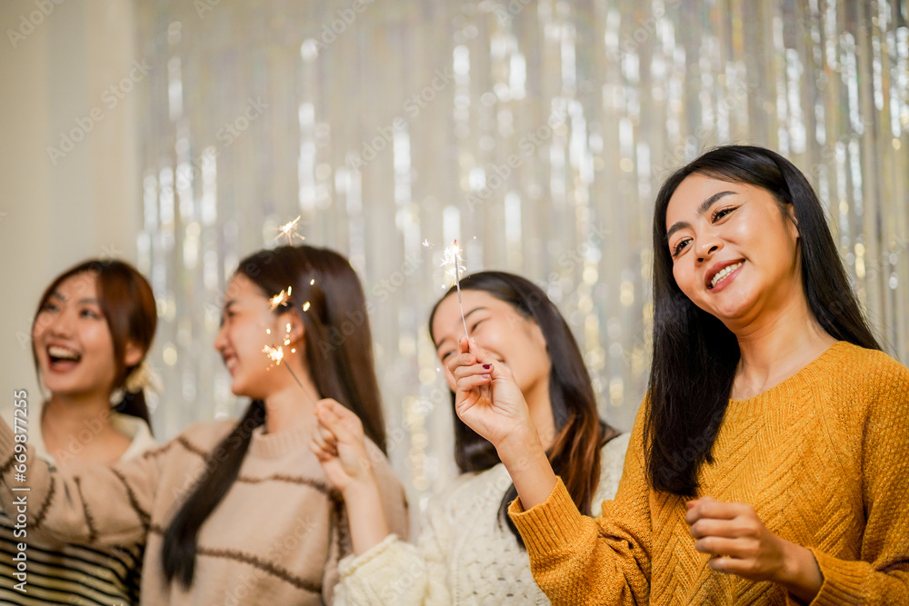 Cheerful friends enjoying home Birthday holiday party. Asian Friends hold lights with sparkling Sparkler celebrating Christmas or New Year eve party.