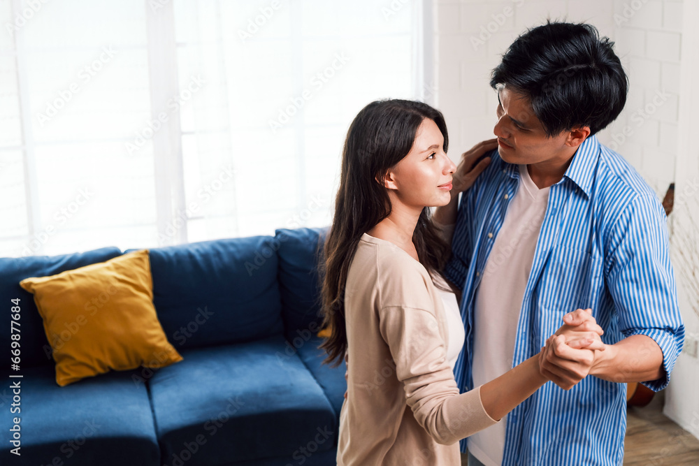 Attractive young Asian couples enjoy having a lovely romantic dance in the living room of the apartment. A family spends quality time together after moving into a new home. Image with copy space. Attractive young Asian couples enjoy having a lovely romantic dance in the living room of the apartment. A family spends quality time together after moving into a new home. Image with copy space.