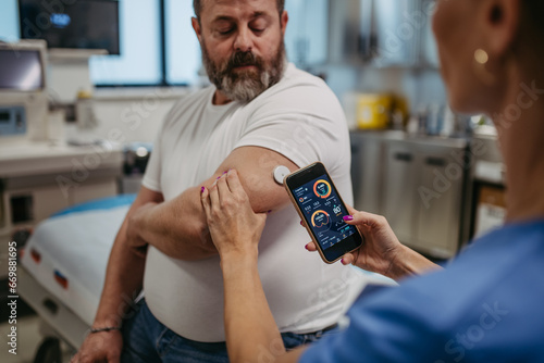 Doctor connecting continuous glucose monitor with smartphone, to check blood sugar level in real time. Obese, overweight man is at risk of developing type 2 diabetes. Concept of health risks of