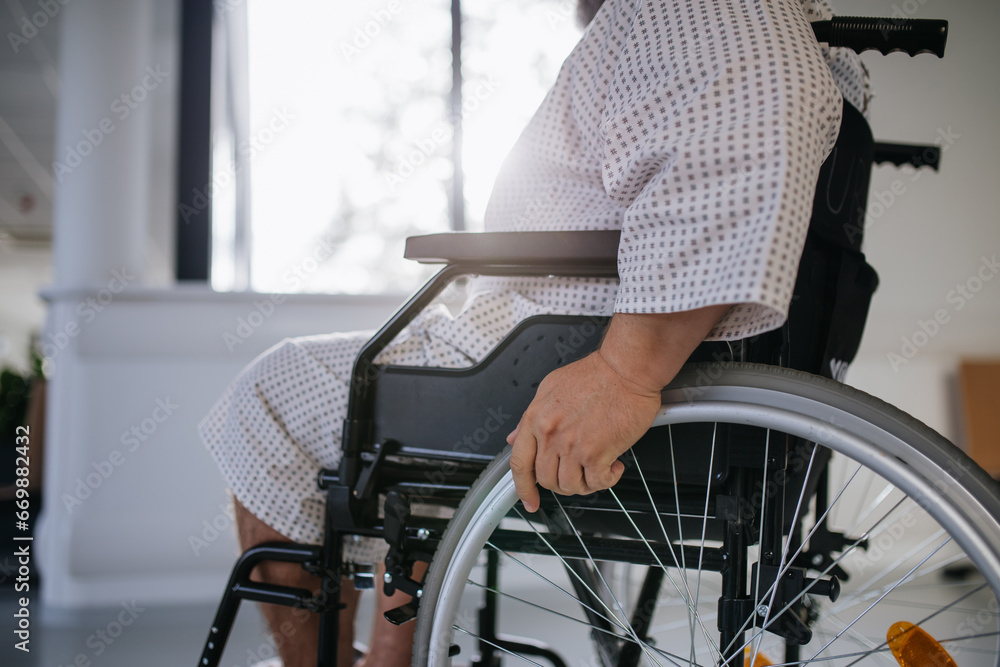 Obraz premium Side view of man in wheelchair. Overweight patient in hospital gown waiting for medical examination in hospital.