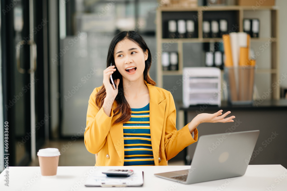 Asian Business woman Talking on the phone and using a laptop with a smile while sitting at office Asian Business woman Talking on the phone and using a laptop with a smile while sitting at office