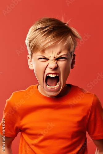 Angry irritated boy on red background. Full of rage. Emotional portrait of an upset preteen boy screaming in anger. Vertical photo.