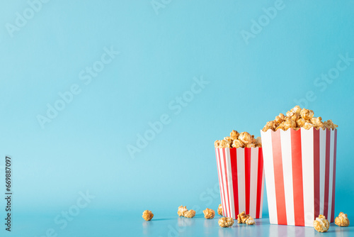 Cinema time with friends and snacks inspiration. Side view perspective picture of a tabletop filled with scrumptious popcorn in striped containers against a soft blue wall, great for movie promo
