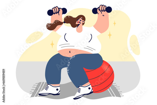 Pregnant woman is doing fitness sitting on large yoga ball and lifting dumbbells above head