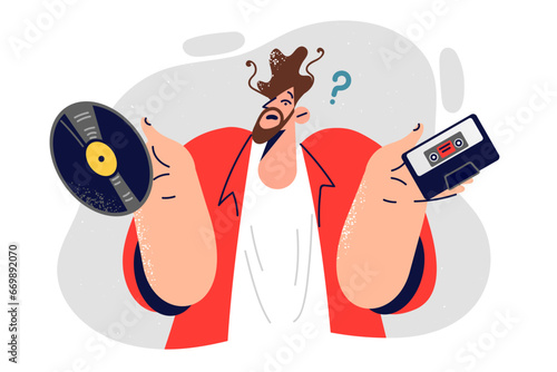 Hipster man holds vinyl record and tape player cassette trying to make choice between analog media