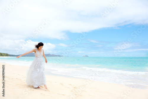 Teen girl in white dress walking barefoot on hawaiian beach
