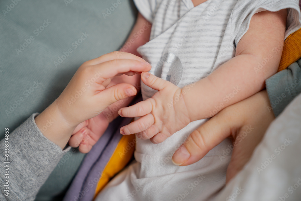 Mother holding little infant newborn small hands and sister also touching brother small infant arms and fingers