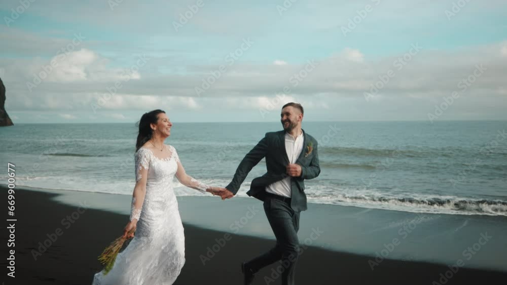 Smiling married couple spending special day on gorgeous black sand beach, listening to the sound of crashing waves, enjoying the beauty of blue sea and sky. High quality 4k footage Smiling married couple spending special day on gorgeous black sand beach, listening to the sound of crashing waves, enjoying the beauty of blue sea and sky. High quality 4k footage