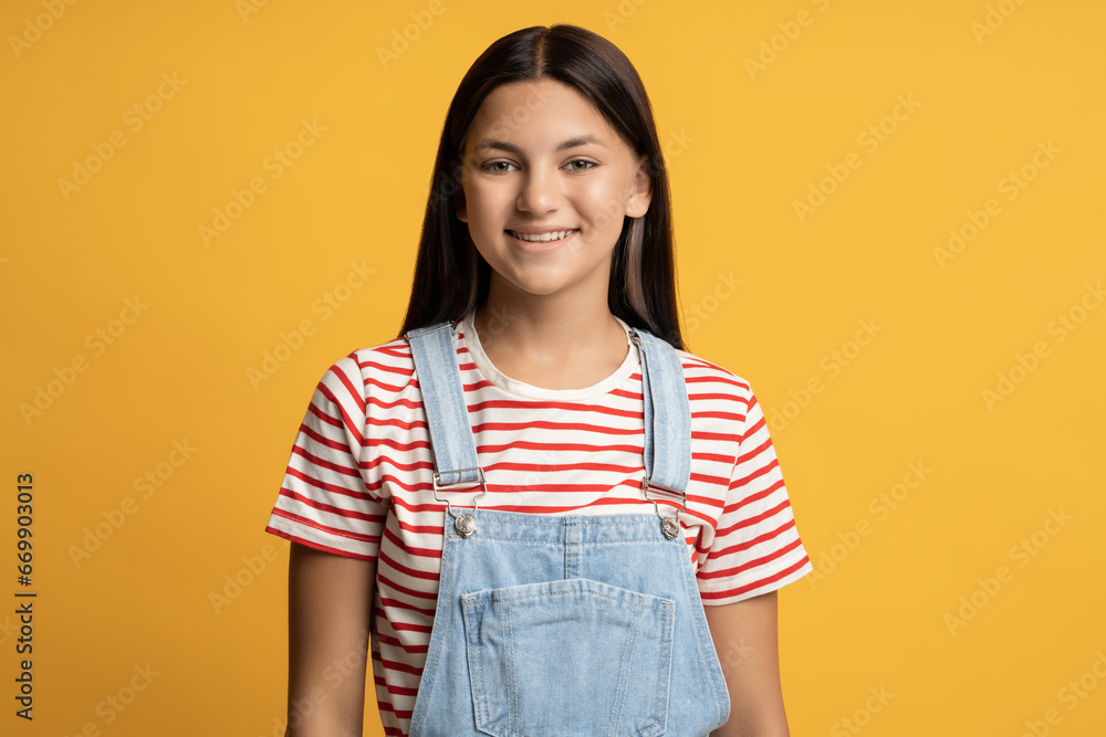 Portrait of happy brunette tanned teen girl isolated on yellow background looking at camera. Smile positive friendly teenager posing on poster with copy space. Advertisement banner marketing concept. Portrait of happy brunette tanned teen girl isolated on yellow background looking at camera. Smile positive friendly teenager posing on poster with copy space. Advertisement banner marketing concept.