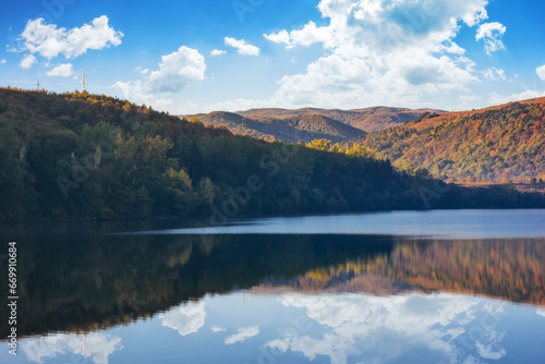 mountainous autumn landscape with lake. nature background with trees on the shore reflecting in the calm water. warm sunny weather in the morning