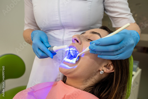 dentist using UV lamp with photopolymer composition for teeth whitening her female patient
