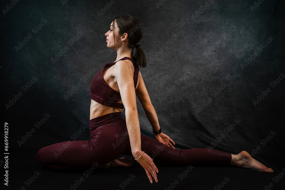 Attractive caucasian slim woman in sport cloth doing yoga stretching at studio black background