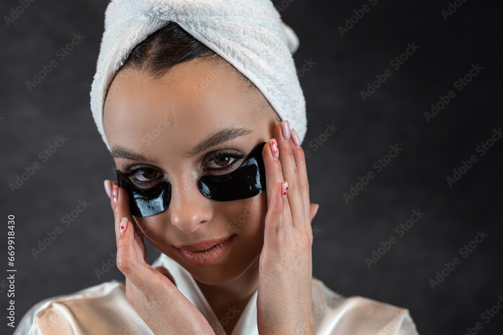 Attractive woman wear towel with eye patches posign at camera isolated on black Attractive woman wear towel with eye patches posign at camera isolated on black