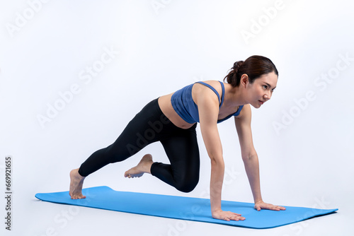 Asian woman in sportswear doing burpee on exercising mat as workout training routine. Attractive girl in pursuit of healthy lifestyle and fit body physique. Studio shot isolated background. Vigorous